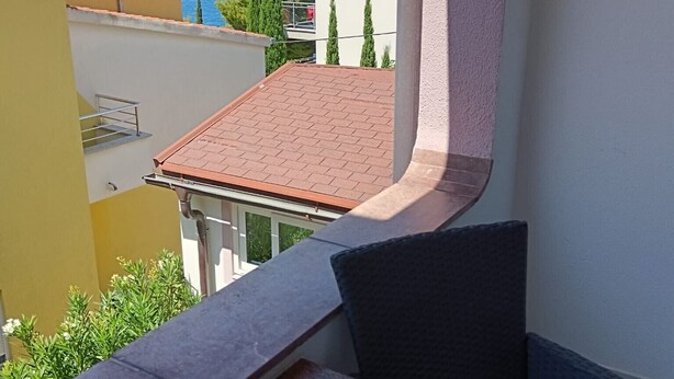A balcony with a table and chair, overlooking a coastal area with buildings and a clear sky. - Guest House Villa Daniel - Two Bedroom Apartment with Balcony (Omis)
