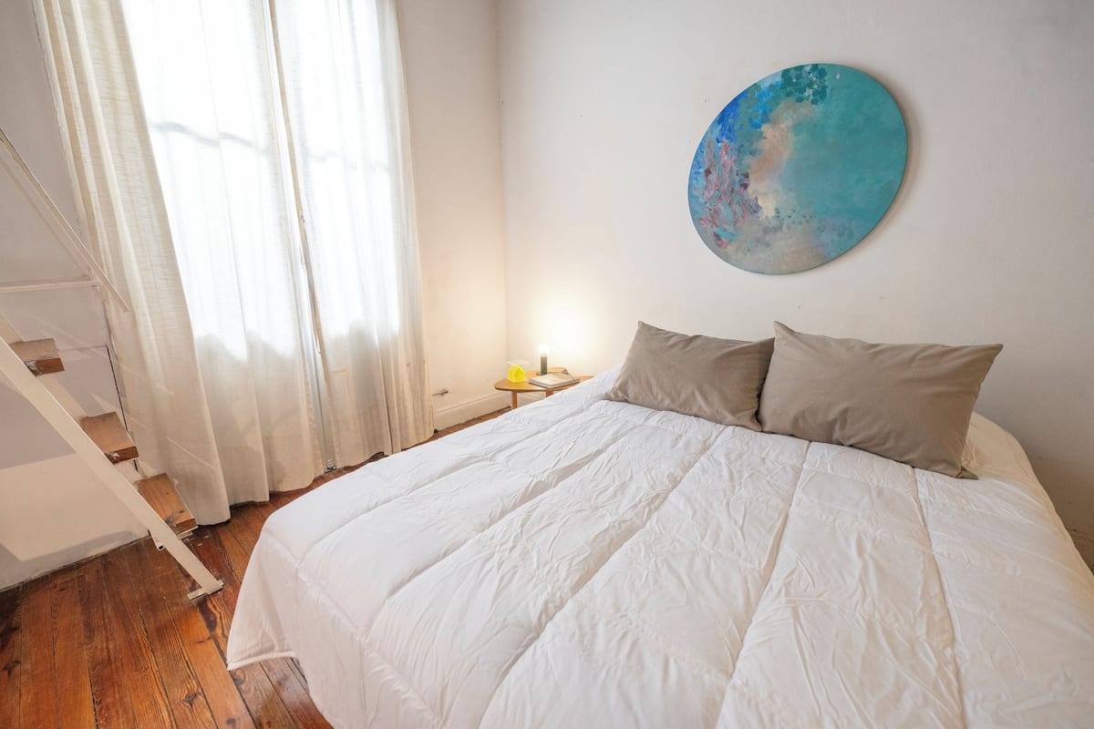 Ein Schlafzimmer mit einem großen Bett, einem Nachttisch mit Lampe, einem Gemälde an der Wand und einer Treppe.
