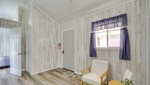 Ein Zimmer mit einer weißen Tür, einem weißen Stuhl, einem Holztisch und einem Fenster mit violetten Vorhängen.