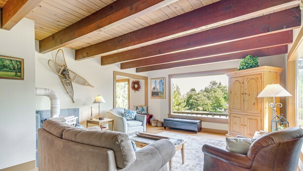 A spacious living room with a high ceiling, wooden beams, a large window with a view of trees, a fireplace, and a cozy seating area. - Langley Forest Cabin w/ Grill < 2 Mi to Downtown! (Langley)