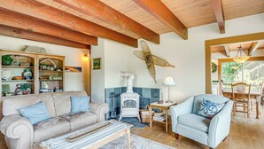 A cozy living room with a sofa, armchair, and a small table. A white stove is in the corner, and there's a large window with a view of greenery. - Langley Forest Cabin w/ Grill < 2 Mi to Downtown! (Langley)