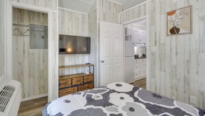 A bedroom with a bed, a dresser, a TV, and a door leading to a kitchen. - Pet-Friendly Picayune Tiny Home Near Space Center! (Picayune)