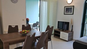 Een moderne woonkamer met een eethoek, een televisie en een klok aan de muur.