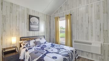 A bedroom with a bed, a nightstand, a wall-mounted heater, and a window with curtains.