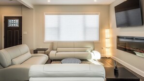 Un salon moderne avec un canapé d’angle, un téléviseur à écran plat fixé au mur et une cheminée.