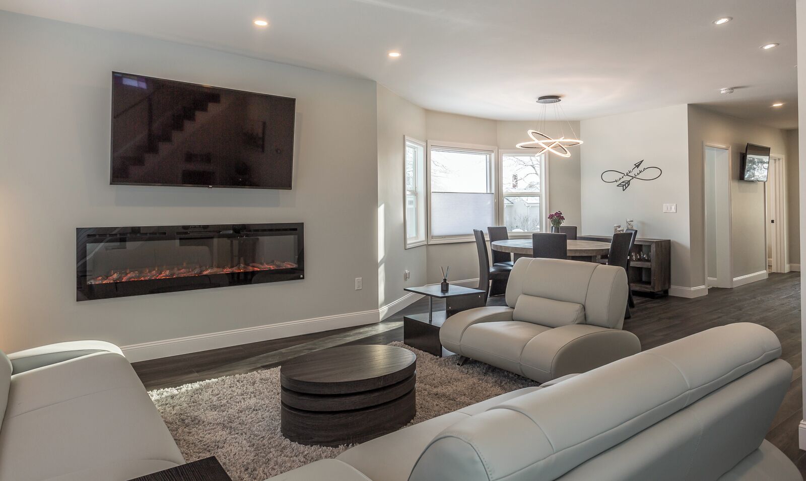 A modern living room with a fireplace, a flat-screen TV, and a dining area with a table and chairs.