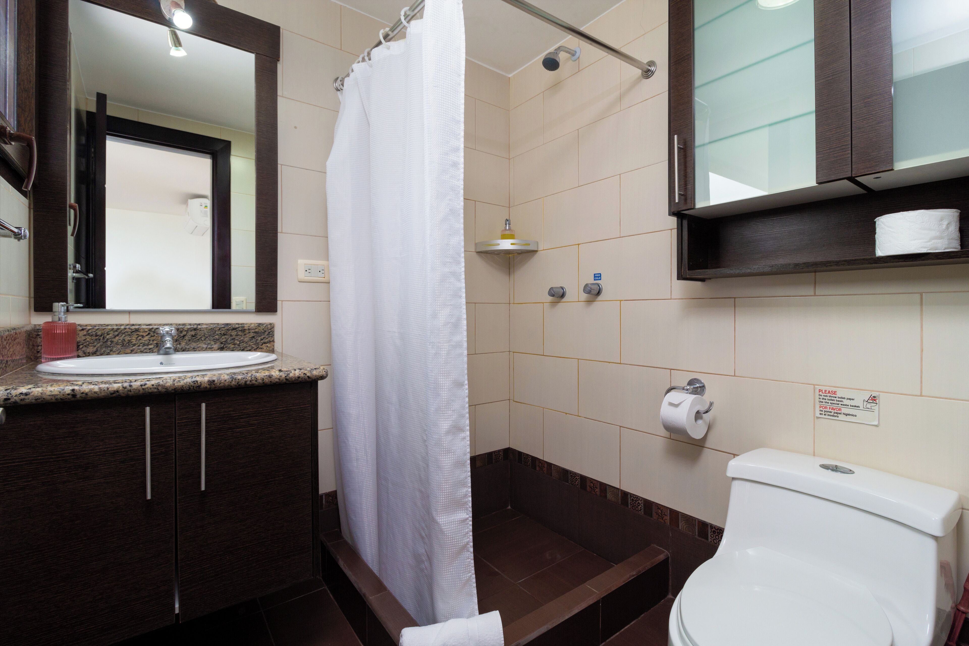 A bathroom with a shower, toilet, sink, and a mirror.