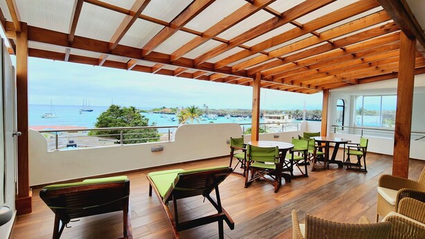 Un área de estar al aire libre, techada, con mobiliario de madera y vista al mar.