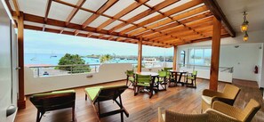 A covered outdoor seating area with wooden furniture and a view of the sea. - BAY VIEW HOUSE  (Puerto Ayora)