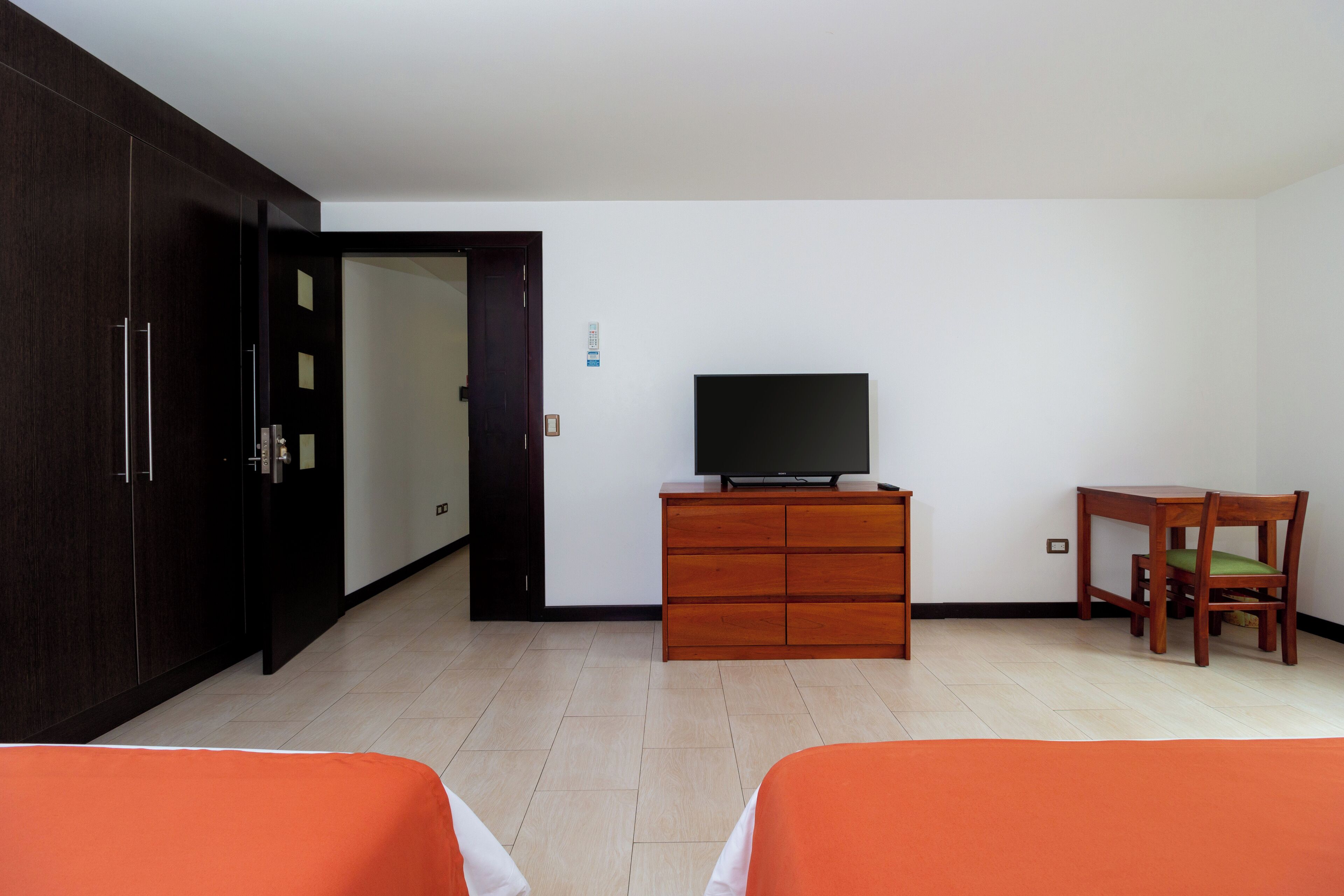 A hotel room with a bed, a TV on a wooden dresser, a chair, and a wardrobe.