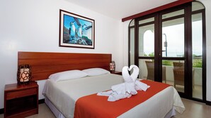 Habitación de hotel con una cama, un cuadro en la pared, una mesita de noche y un balcón con sillas.