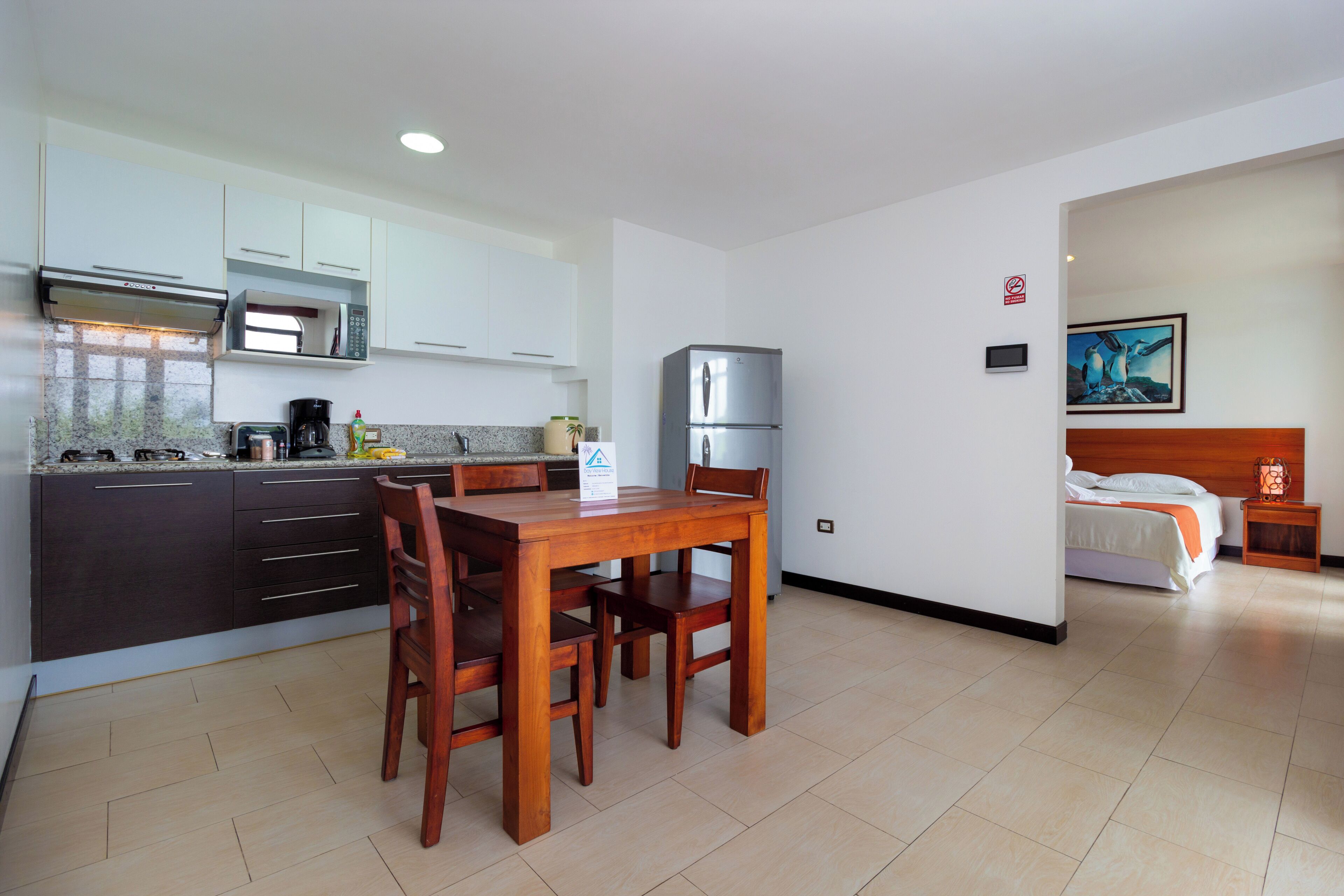 A modern kitchen with a dining table and chairs, a refrigerator, and a bed in the adjacent room.