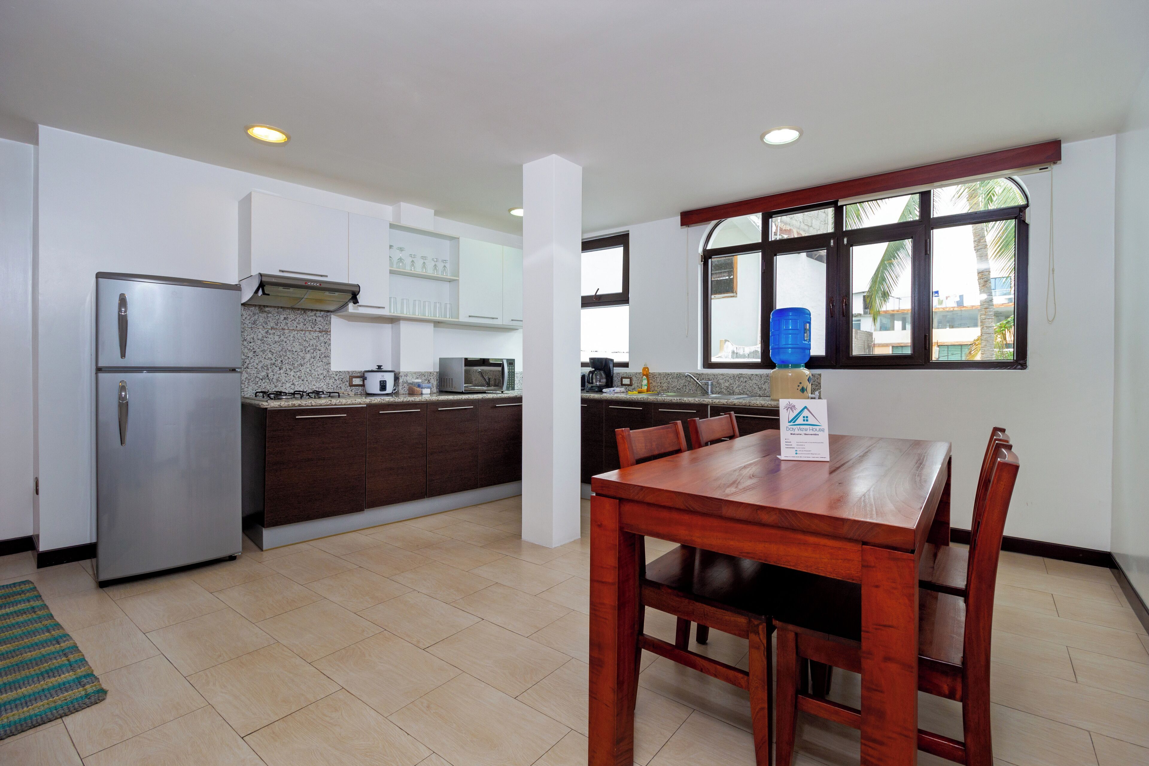A modern kitchen with a refrigerator, stove, and microwave. There is a dining table with chairs and a window with a view.