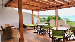 Un espacio al aire libre cubierto con piso de madera, sillas acolchadas verdes y una mesa redonda.