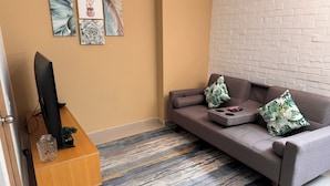 A living room with a grey sofa, two decorative pillows, a TV on a wooden stand, and a patterned rug. - Exclusivo Apartamento en el Poblado by Hoost 705 (Medellín)