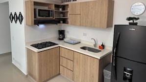 A modern kitchen with wooden cabinets, a black refrigerator, a microwave, a coffee maker, and a clock on the wall. - Exclusivo Apartamento en el Poblado by Hoost 705 (Medellín)