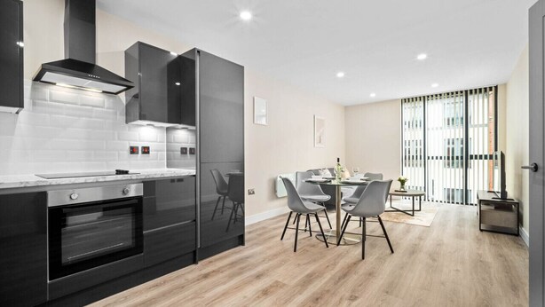 A modern kitchen with dark cabinetry, a built-in oven, and a dining area with a table and chairs.