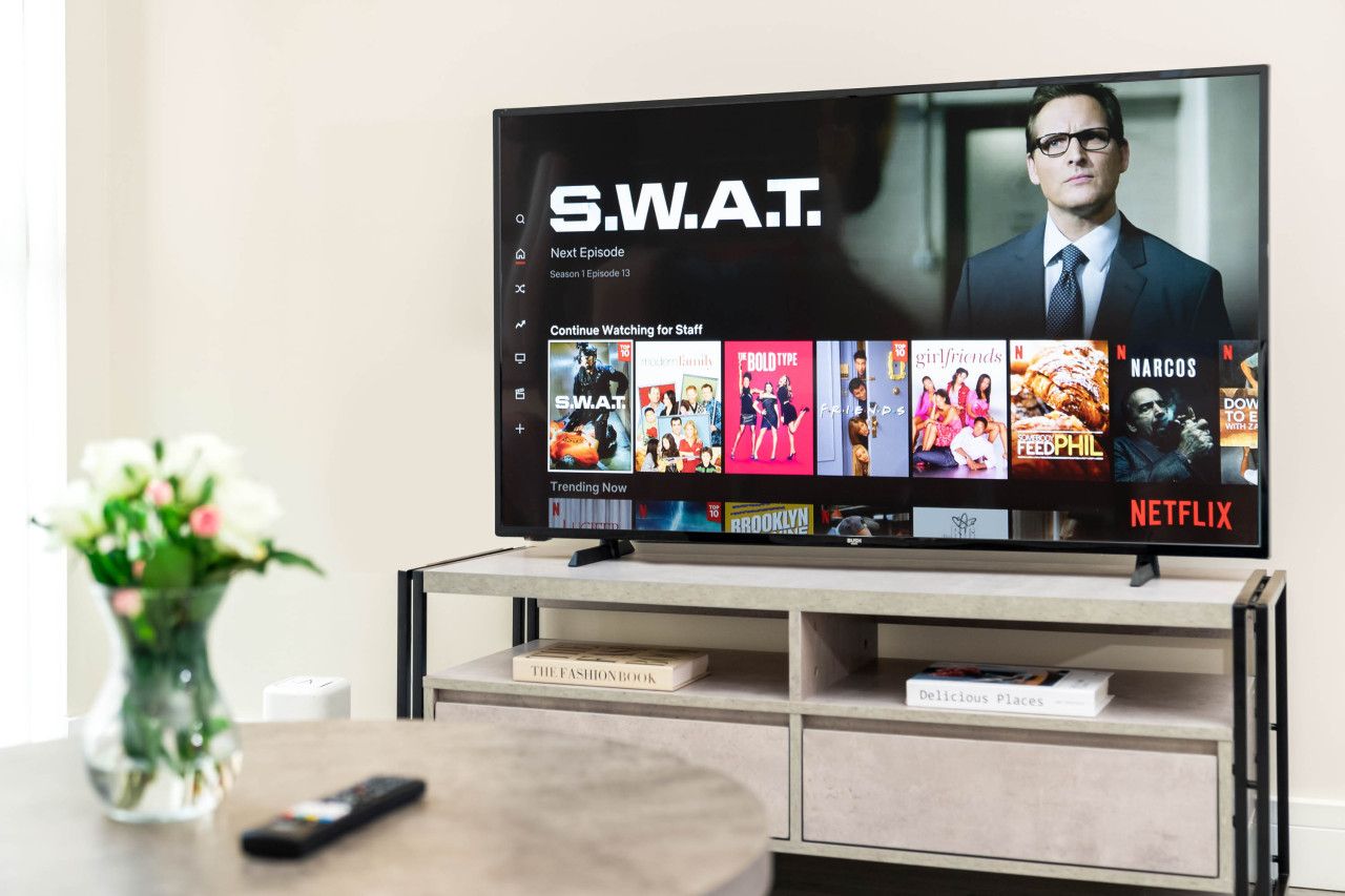 A television displaying a streaming service interface with various shows and a remote control on a table.