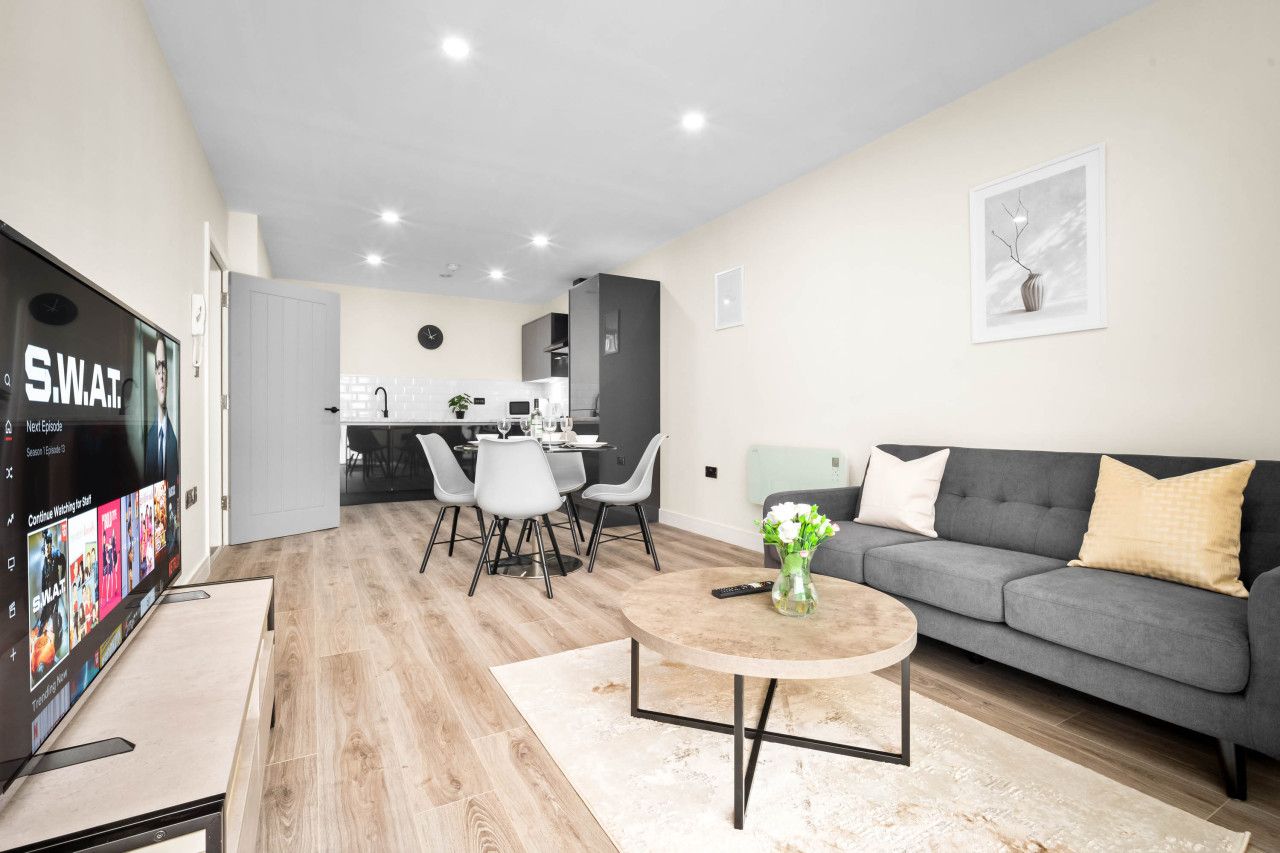 Ein modernes Wohnzimmer mit einem grauen Sofa, einem runden Couchtisch und einem Essbereich mit weißem Tisch und Stühlen.