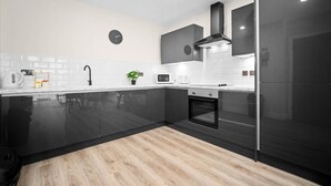 A modern kitchen with black cabinets, a microwave, a kettle, and a clock on the wall.