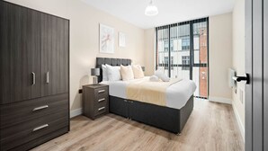 A modern bedroom with a bed, wardrobe, bedside table, and a view of a building through a window.
