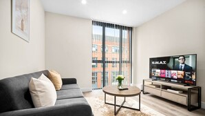 A modern living room with a grey sofa, a coffee table, and a TV on a stand.