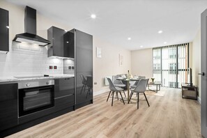 A modern kitchen with dark cabinetry, a built-in oven, and a dining area with a table and chairs. - Stylish 2 Bed Apartment - Smart TV - WIFI -  Jewellery Quarter (Birmingham)