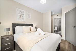 A modern hotel room with a large bed, bedside tables, a nightstand, and a bathroom visible through an open door. - Stylish 2 Bed Apartment - Smart TV - WIFI -  Jewellery Quarter (Birmingham)