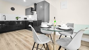 A modern kitchen with a dining area, featuring a glass table, grey chairs, and a black microwave. - Luxury 2 Bed Apartment - Smart TV - WIFI -  Jewellery Quarter (Birmingham)