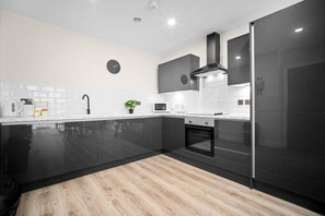 A modern kitchen with black cabinetry, a microwave, a stove, and a clock on the wall. - Stylish 2 Bed Apartment - Smart TV - WIFI -  Jewellery Quarter (Birmingham)