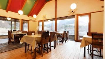 A dining area with multiple tables and chairs, large windows, and a wooden ceiling.