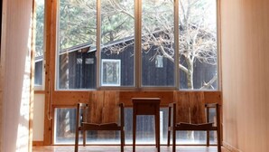 Une pièce dotée d’une grande fenêtre, de chaises en bois et offrant une vue sur des arbres et une structure en bois à l’extérieur.