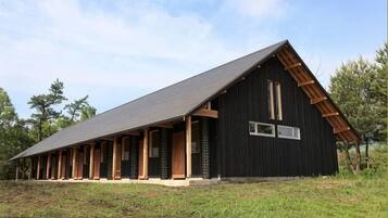 A large black barn with a sloped roof and wooden beams, surrounded by grass and trees.