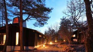 Una baita rustica con un sentiero sterrato che vi conduce, circondata da alberi.