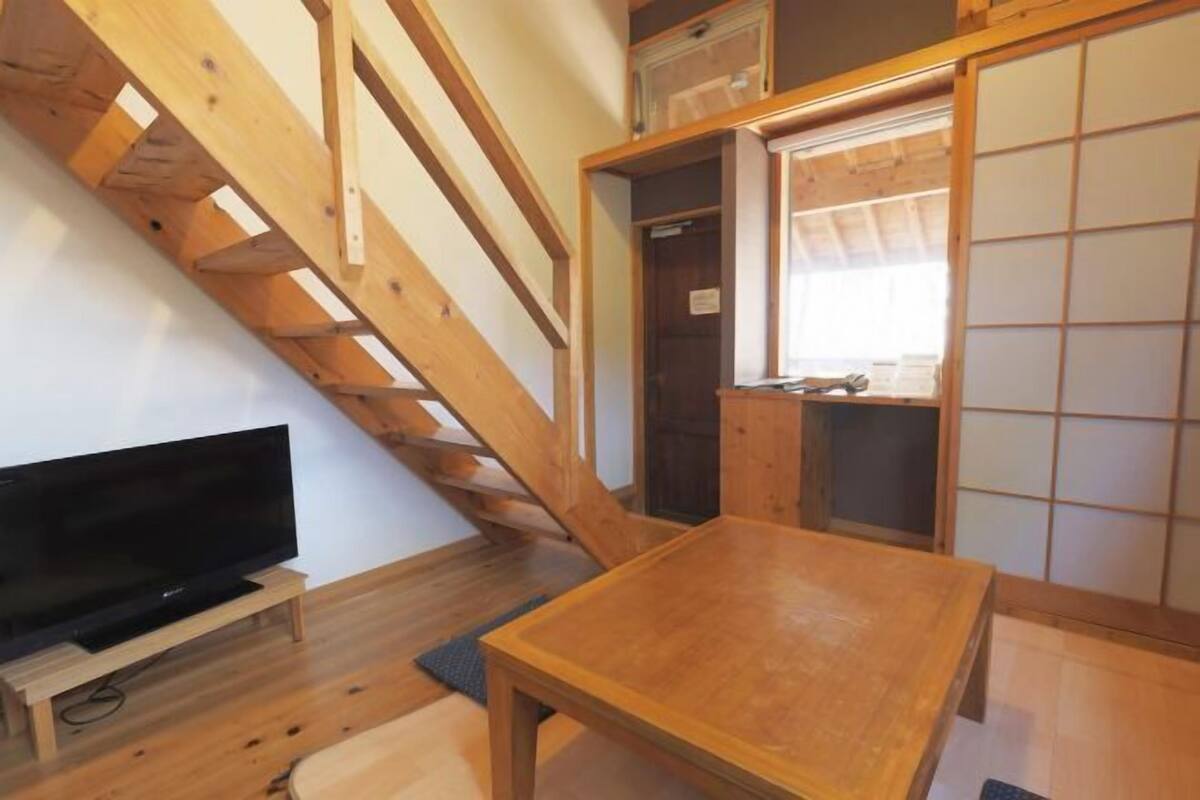 Un escalier en bois mène à une pièce où se trouve un téléviseur posé sur un meuble et une table en bois.