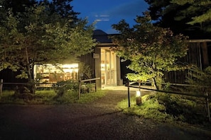 A building with a well-lit entrance, surrounded by trees and a gravel path. - Lodge Toranoyu (Kokonoe)