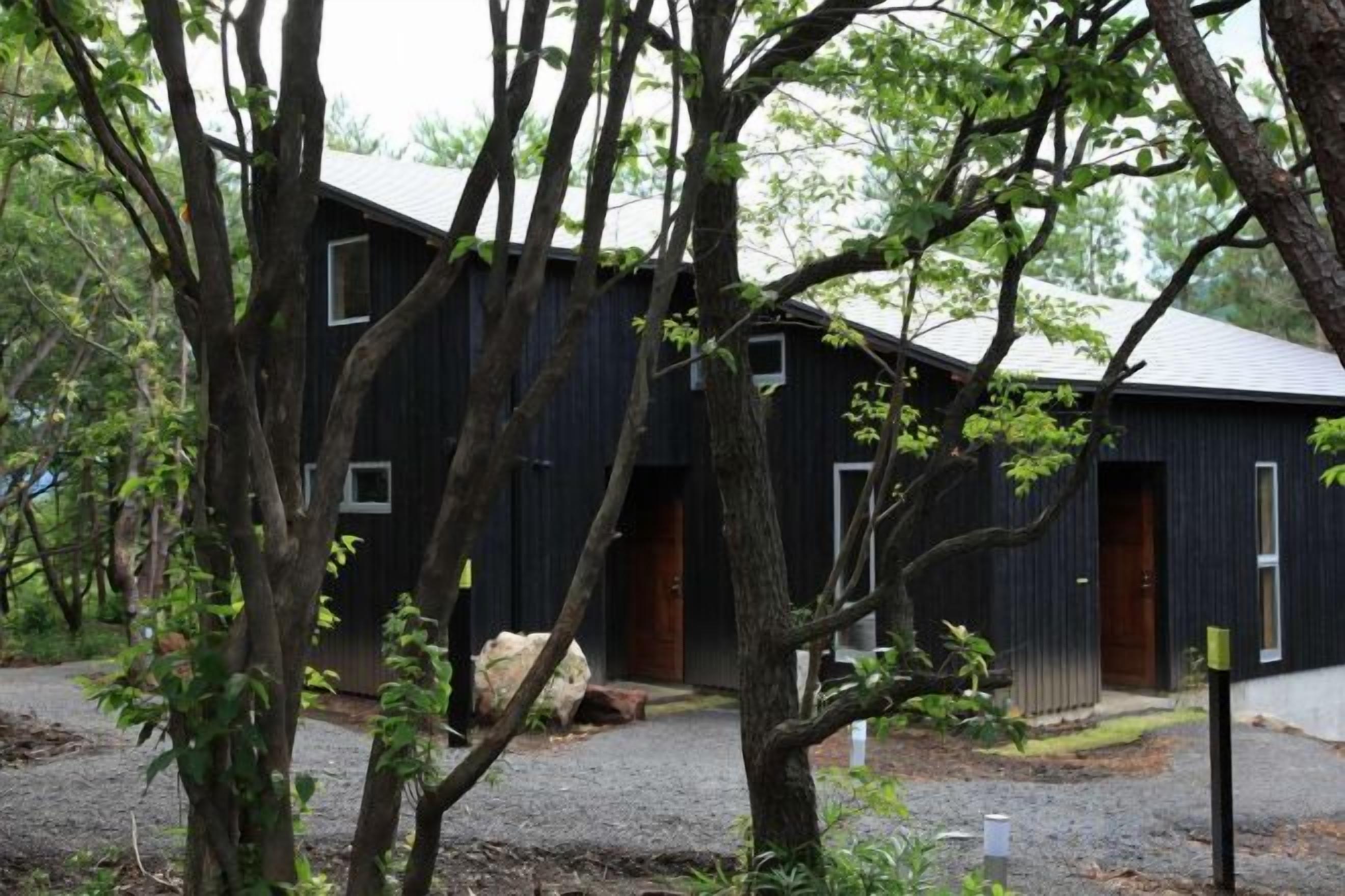 A rustic building with multiple windows and a door, surrounded by trees.