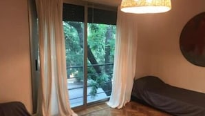 A room with a herringbone wooden floor, a large window with curtains, and a round wall decoration. - Art House Carranza  (Buenos Aires)