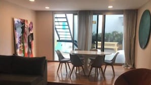 A modern living room with a sofa, a dining table with chairs, and a large window with a view of the outdoors. - Art House Carranza  (Buenos Aires)