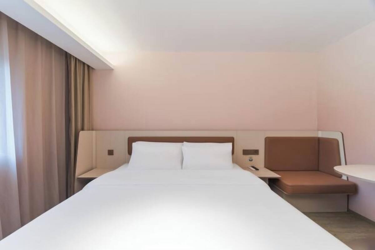 Une chambre d’hôtel avec un grand lit, une table de chevet, un coin salon et une fenêtre avec des rideaux.