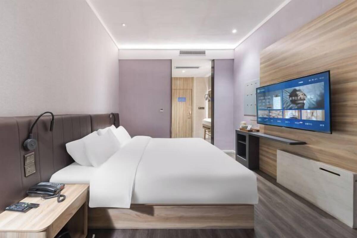 Une chambre d’hôtel moderne équipée d’un lit, d’une table de chevet avec un téléphone et d’un téléviseur fixé au mur.