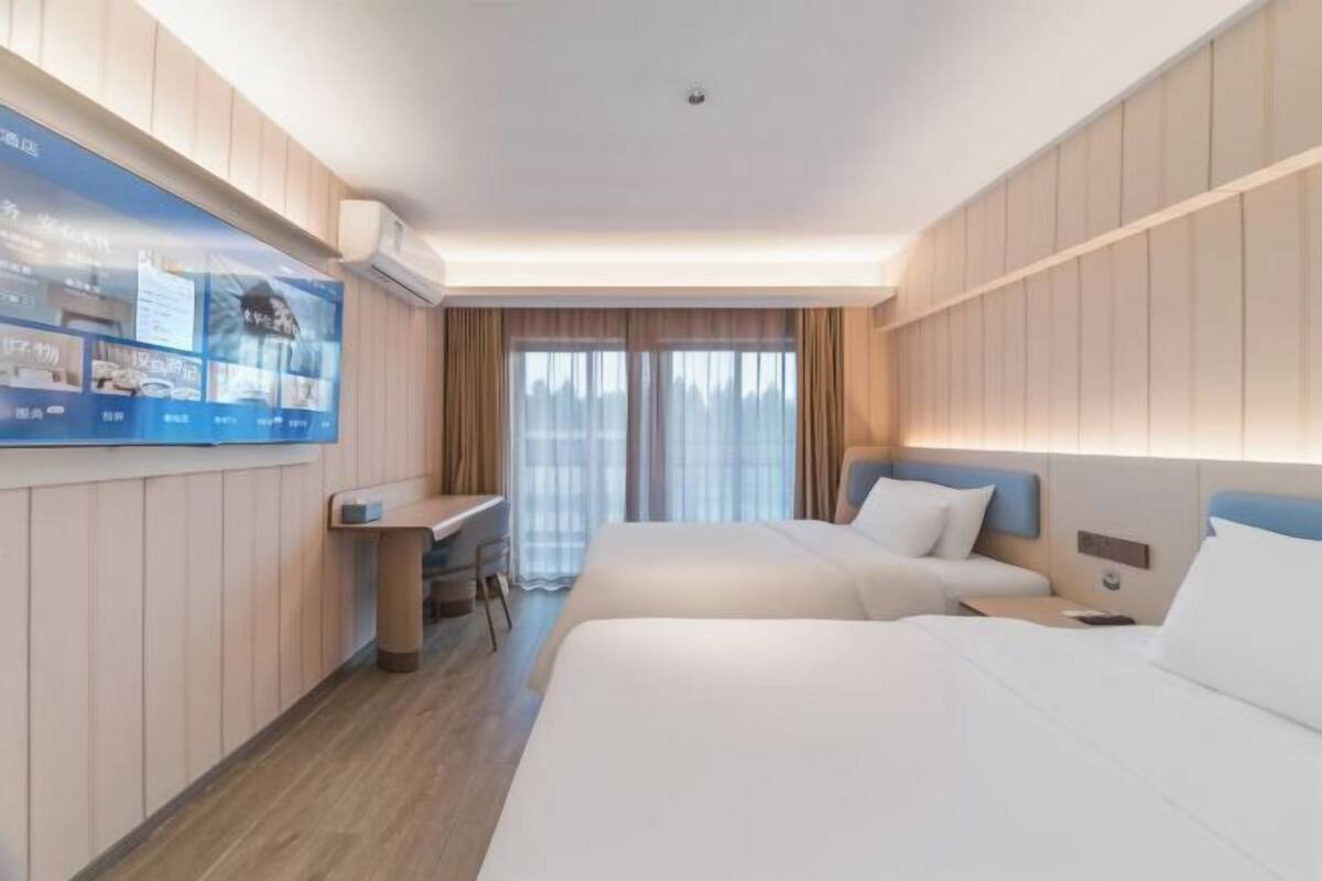 Une chambre d’hôtel avec deux lits, un bureau, une télévision et une fenêtre avec des rideaux.