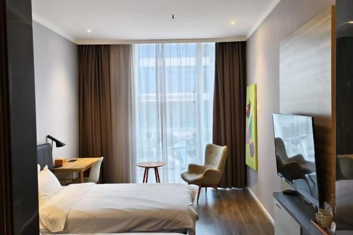 Une chambre d’hôtel avec un lit, un bureau, une chaise, une télévision et une grande fenêtre avec des rideaux.