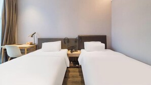 A hotel room with two single beds, a desk with a chair, a bedside table with headphones, and a small table with a lamp. - HanTing Hotel (Guangzhou Tianhe Bus Station) (Guangzhou)