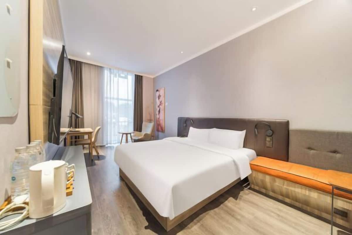 Une chambre d’hôtel avec un grand lit, un bureau avec une chaise, une télévision et une fenêtre avec des rideaux.