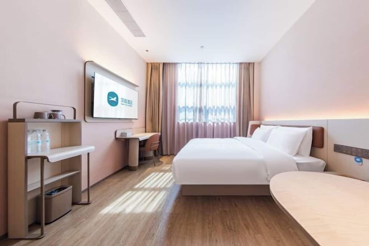 Une chambre d’hôtel avec un lit, un bureau, une chaise, une télévision et une fenêtre avec des rideaux.
