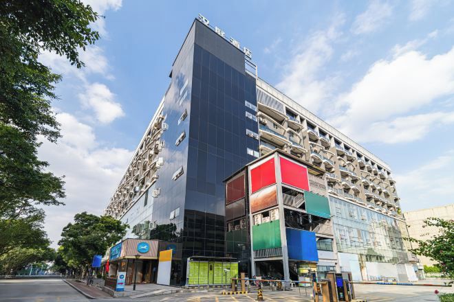 Un edificio de varios pisos con fachada de vidrio moderna, un estacionamiento y varios locales comerciales en la planta baja.