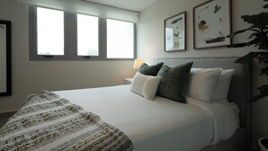 Un dormitorio ordenado con una cama grande, una mesita de noche con lámpara y dos cuadros enmarcados en la pared.