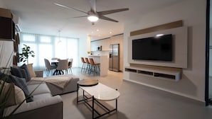 Una sala de estar moderna con un sofá, una mesa de centro y un televisor. Hay un comedor con sillas y una mesa.