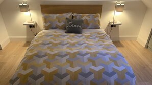 A neatly made bed with a geometric patterned bedspread, two bedside lamps, and a pillow with the word "Dream" on it. - Delightful studio with WiFi in Ballyvaughan (Ballyvaughan)
